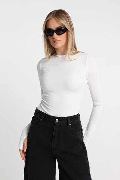 A close-up studio shot of a model wearing the white Rumi long-sleeve baby tee, accessorized with black rectangular sunglasses to showcase the high scooped neckline and fitted silhouette.