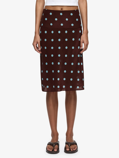 A cropped front shot focusing on the lower half of the body, emphasizing the mid-rise fit of the wide waistband against the waist, the regular spacing of the polka dot print, and the airy, lightweight drape of the skirt over the legs.