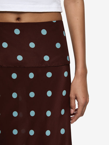 A close-up detail shot highlighting the textured weave of the brown silk-blend fabric, the light blue polka dot print pattern, the subtle seam line construction of the wide waistband, and the edge finish of the cropped white top.