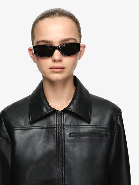 Close-up studio portrait highlighting the structured collar, matte black zipper, and smooth faux leather texture of the Bec + Bridge Saphira Cropped Jacket in Black.