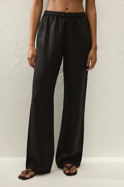 Close-up front view of a model wearing the black trousers, highlighting the high-rise elasticated waistband and straight-leg drape.