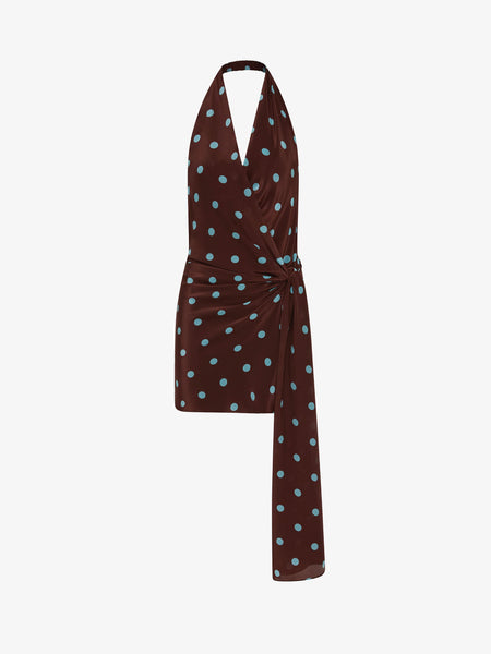 A clear product-only photograph isolating the Mathilde Halter Mini Dress against a plain background. The shot highlights the brown fabric with light blue polka dots, the plunging halter neckline, and the fluid wrap-style skirt featuring a gathered side-tie fabric panel.