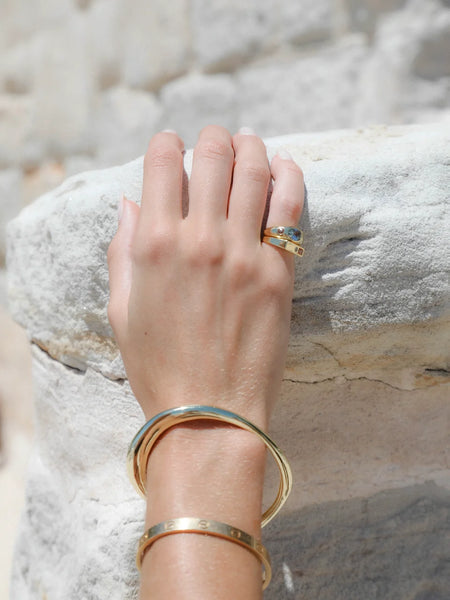 Close-up view of a hand wearing the stacked rings resting on a textured white surface, complemented by a gold bangle and cuff bracelet.