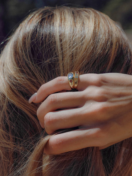 Close-up of a hand with stacked gold rings resting against blonde hair, featuring the Jessica ring and a stone-set domed ring.