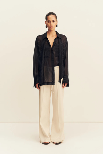 Full-length front studio shot of a model wearing the relaxed-fit Shona Joy Irving Polka Dot Sheer Shirt in Black Polka Stripe paired with cream wide-leg trousers.
