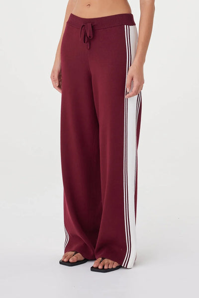 A three-quarter close-up shot prioritizing the side paneling of the trousers. This view cleanly highlights the wide, cream-colored sporty contrast stripe flanked by fine merlot lines.