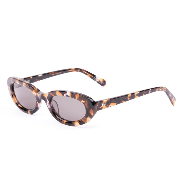 Three-quarter studio view of the Sito Shades Lourdes oval sunglasses in pebble tort highlighting the smooth acetate rim and solid grey lenses.