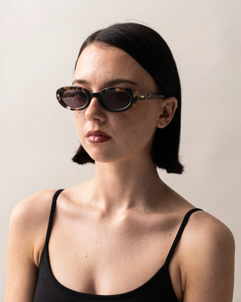Three-quarter portrait view of a model styled in the Sito Shades Lourdes oval sunglasses in pebble tort with grey Cat 3 lenses against a neutral backdrop.