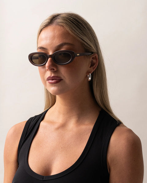 Three-quarter portrait of a blonde model wearing the Sito Shades Lourdes oval sunglasses in translucent milky coco brown with light brown lenses.