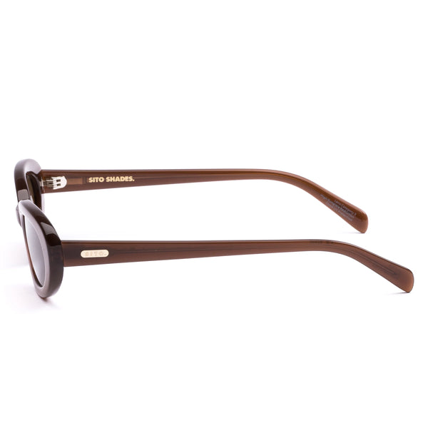 Side profile studio image of the Sito Shades Lourdes oval sunglasses in milky coco brown featuring slim acetate temples and gold-toned brand logo detailing.