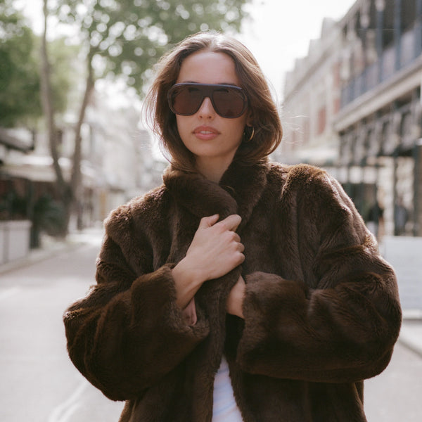 Outdoor street style portrait of a brunette model wearing a plush brown faux fur coat and oversized Sito Shades Paloma aviator sunglasses in translucent milky coco acetate.