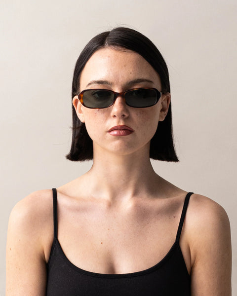 Front portrait of a dark-haired model with a blunt bob wearing the Sito Shades Roux sunglasses in Classic Tort styled with a black camisole top against a light grey background.