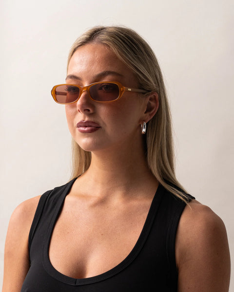 Three-quarter portrait of a blonde model wearing the Sito Shades Roux sunglasses in translucent caramel orange acetate with light brown lenses.