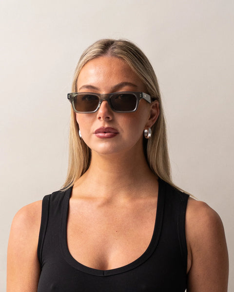 Front portrait of a blonde model wearing the Sito Shades Vincent rectangular sunglasses in translucent Nori green acetate styled with a black tank top and silver hoop earrings.