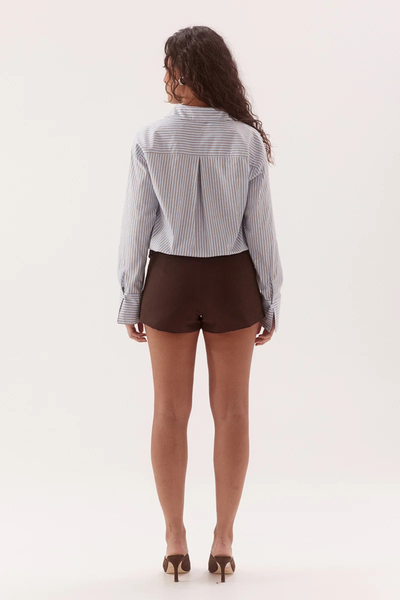 Full-length studio back view of a model wearing a blue and brown striped shirt showing the back yoke pleat, dropped shoulder seams, and relaxed fit paired with dark brown tailored shorts.
