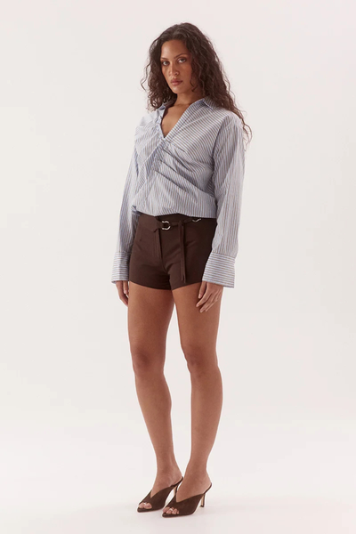 Studio three-quarter side shot of a model wearing a blue and brown striped fixed-wrap cotton-blend shirt with wide cuffs and a deep open placket, paired with brown belt-detailed shorts.