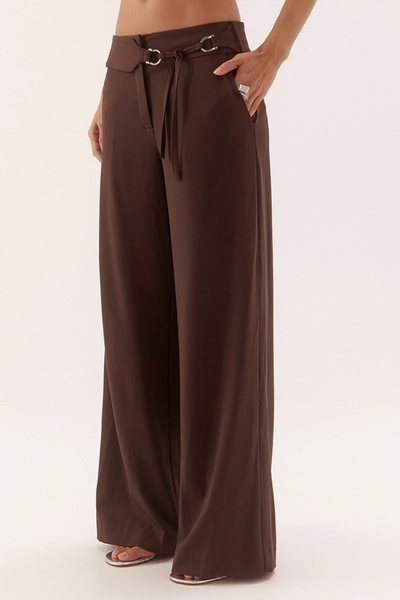 Three-quarter studio side view of a model with a hand in her pocket wearing dark chocolate brown wide-waistband tailored trousers with a straight-leg cut.