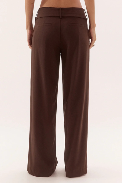 Rear studio view from the waist down of a model wearing mid-rise dark chocolate brown tailored trousers highlighting the wide waistband, belt loops, and back welt pockets.