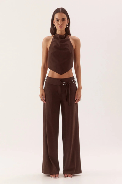 Full-length studio front view of a model wearing a dark chocolate brown high-neck cowl apron top with a V-shaped pointed hem, styled with matching wide-leg trousers.