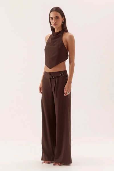 Three-quarter studio front view of a model wearing a dark chocolate rayon-blend apron top with a soft cowl high neck and asymmetric V-hem, paired with matching straight-leg trousers.