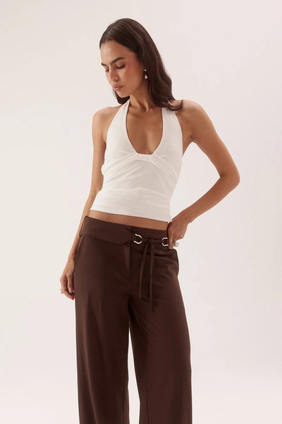 Three-quarter studio portrait of a model looking down while wearing a chalk white stretch mesh halter top with waist gathering and a deep scoop neckline.
