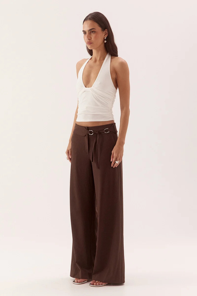 Full-length studio three-quarter front view of a model wearing a chalk white halter neck top with front bust tuck details, paired with wide-leg dark brown trousers.