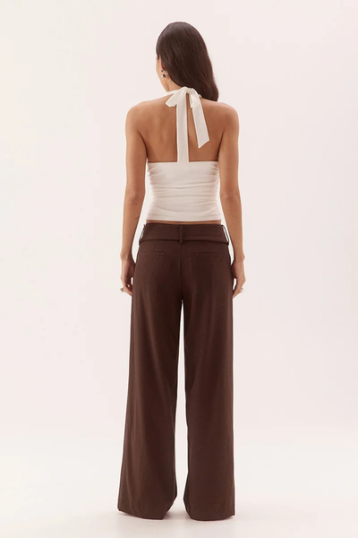 Full-length studio back view of a model wearing a chalk white ribbed halter top showing the thick back neck tie closure and straight back edge, styled with wide-leg chocolate brown pants.