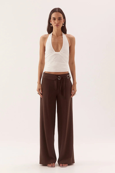 Full-length studio front view of a model wearing a chalk white textured rib halter top featuring front neckline tucks and side bodice gathering, paired with dark brown tailored wide-leg trousers.