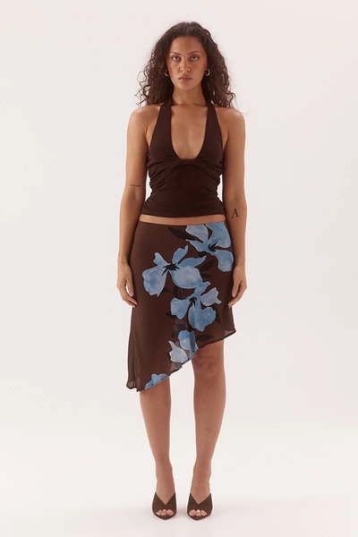 Full-length studio front view of a model wearing a dark chocolate brown ribbed halter neck top with front bust tucks and subtle body-contouring gathers, paired with a printed asymmetrical mesh skirt.