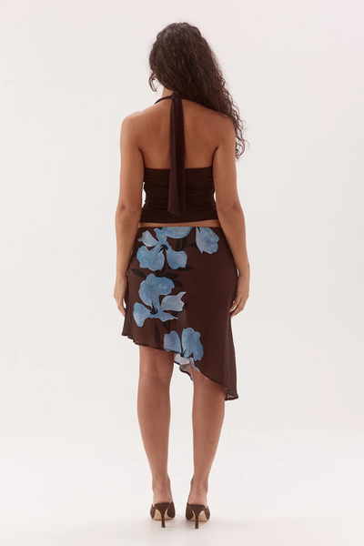 Full-length studio back view of a model wearing a dark chocolate brown halter top highlighting the trailing back neck ties and straight back edge, paired with an asymmetrical brown floral skirt.