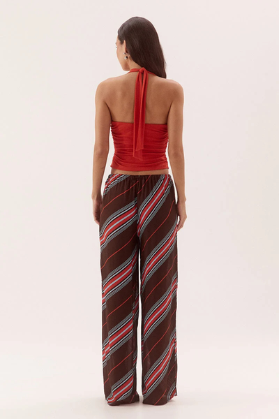 Full-length studio rear view of a model wearing a vermilion red stretch mesh halter top highlighting the trailing back neck ties, straight back edge, and side waist gathers, styled with striped wide-leg pants.