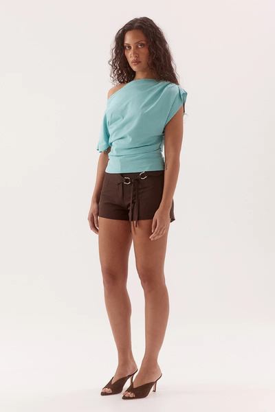 Full-length studio three-quarter view of a model wearing a glacier blue multi-wear boat neck cotton top styled off-the-shoulder, dark brown belt-detailed shorts, and dark brown heels.