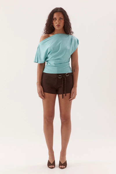 Studio full-length front view of a model wearing a glacier blue pure cotton tee styled asymmetrically off the right shoulder, paired with dark brown tailored shorts and heels.