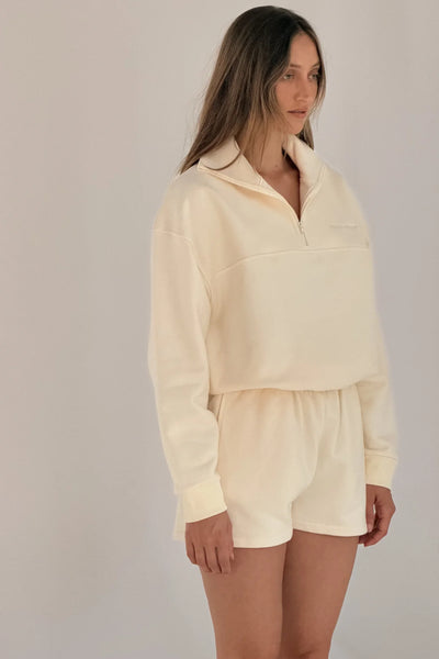 Three-quarter studio view of a model wearing the collared quarter-zip Zulu & Zephyr Sport Sweat Shirt Fleece in Cream with matching shorts.