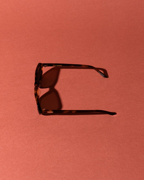 Side profile studio image of the Sito Shades Roux sunglasses in classic tortoiseshell acetate displaying the temple arm casting a shadow on a terracotta background.