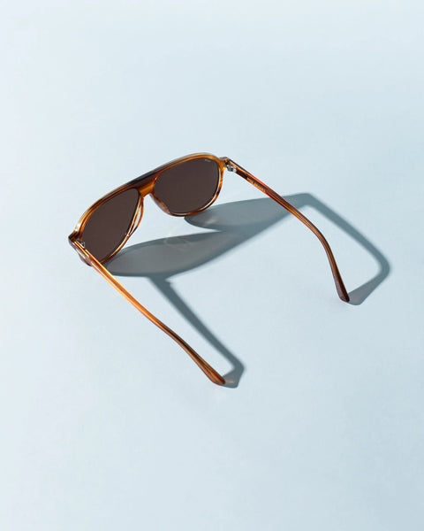 Sito Shades Bobbi in Tangelo featuring translucent orange acetate aviator frames with dark brown lenses displayed on a light blue background with direct sunlight casting sharp shadows.