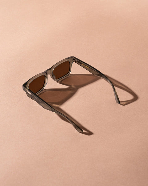 Top-down studio shot of the Sito Shades Vincent sunglasses in translucent Nori green acetate displaying dark brown lenses and extended temple arms against a warm beige surface.