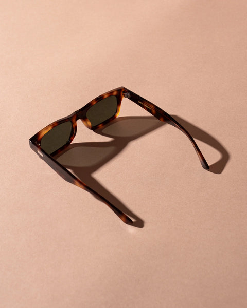Overhead studio shot of the Sito Shades Vincent sunglasses in translucent classic tortoiseshell acetate with dark grey lenses and open temple arms on a warm beige backdrop.