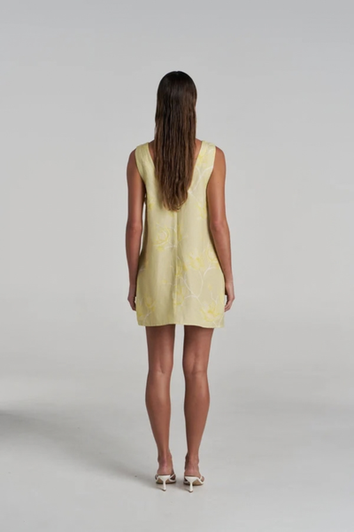 Studio rear view of a model wearing the yellow floral mini dress, showcasing the relaxed silhouette and scoop back.