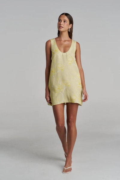 Full-length front studio view of a model walking towards the camera while wearing the relaxed-fit yellow and white floral mini dress.