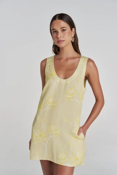 Close-up studio front view of a model wearing the magnolia yellow and white floral mini dress, highlighting the scoop neckline and side pockets.