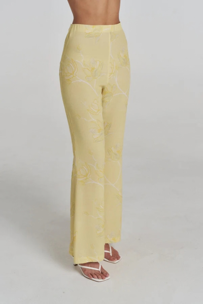 Close-up studio side profile view of a model wearing the yellow and white floral crepe pants, highlighting the fitted silhouette through the hips and slight flare at the hem.