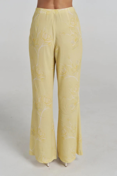 Studio rear view of a model wearing the yellow floral viscose-rayon crepe pants, showcasing the fitted waistband and tailored drape.