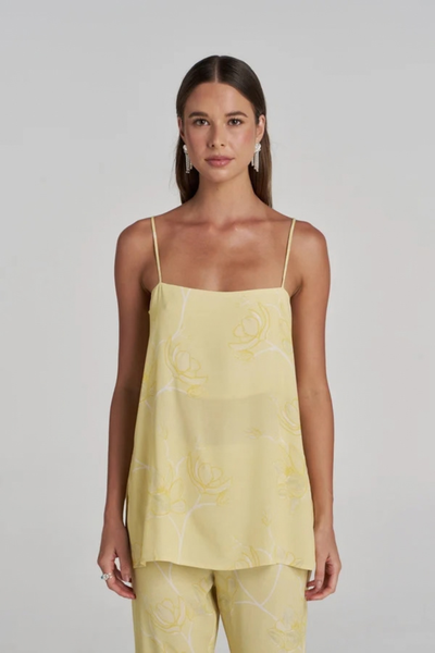 Close-up studio front view of a model wearing the yellow and white floral tunic top with thin spaghetti straps, paired with matching trousers and drop earrings.