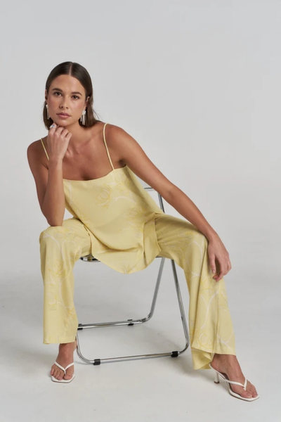 Studio portrait of a model sitting on a chair with one hand resting on her chin, wearing the yellow floral tunic set.