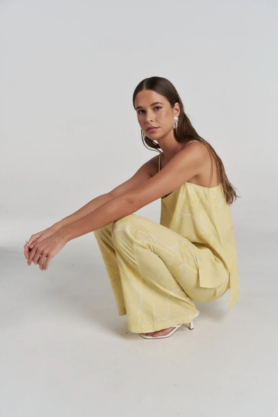 Studio side view of a model squatting down, showcasing the fluid movement and high side slits of the magnolia yellow floral tunic top.