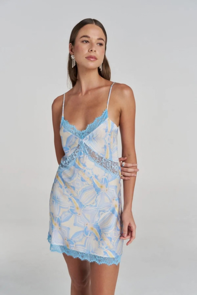 Close-up studio front view of a model wearing the blue patterned slip dress, highlighting the V-neckline, sheer lace side inset, and blue lace trim.