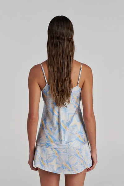 Studio side profile view of a model wearing the blue and white Orchid Prism patterned camisole with blue lace trim, paired with a matching mini skirt.