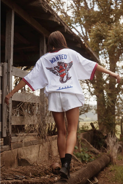 Back view of a model wearing the Sabbi The Very Oversized Flying Mermaid Tee in White, featuring the bold "Wanted & Wild" winged graphic print.