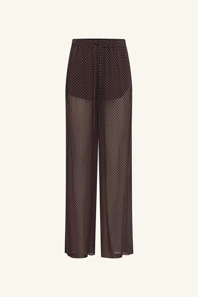 A warm-toned campaign portrait of the model modeling the sheer polka dot pants, showcasing the garment's resort-ready styling potential and how the print translates in natural studio lighting.